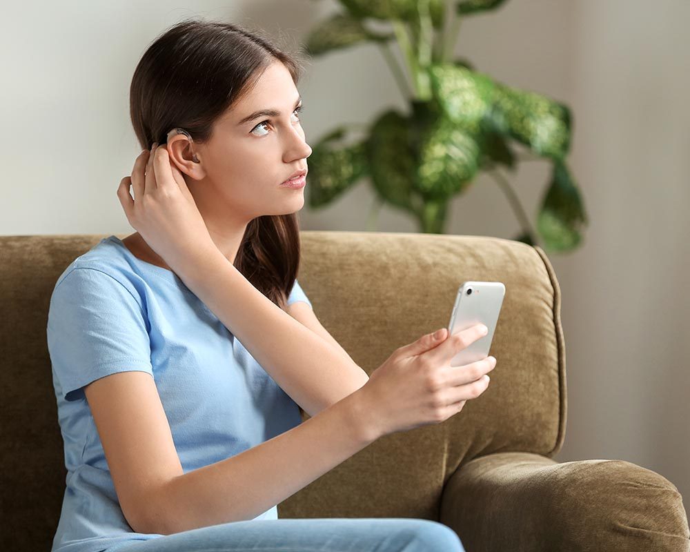Young woman with hearing aid and mobile phone at home